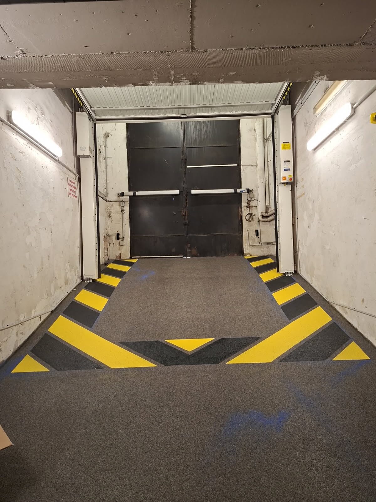 Marquage signalétique jaune et noir sur sol résine PUMA saupoudré dans une rampe de garage